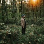 A man in a jacket stands contemplatively in a sunlit forest, embracing nature.
